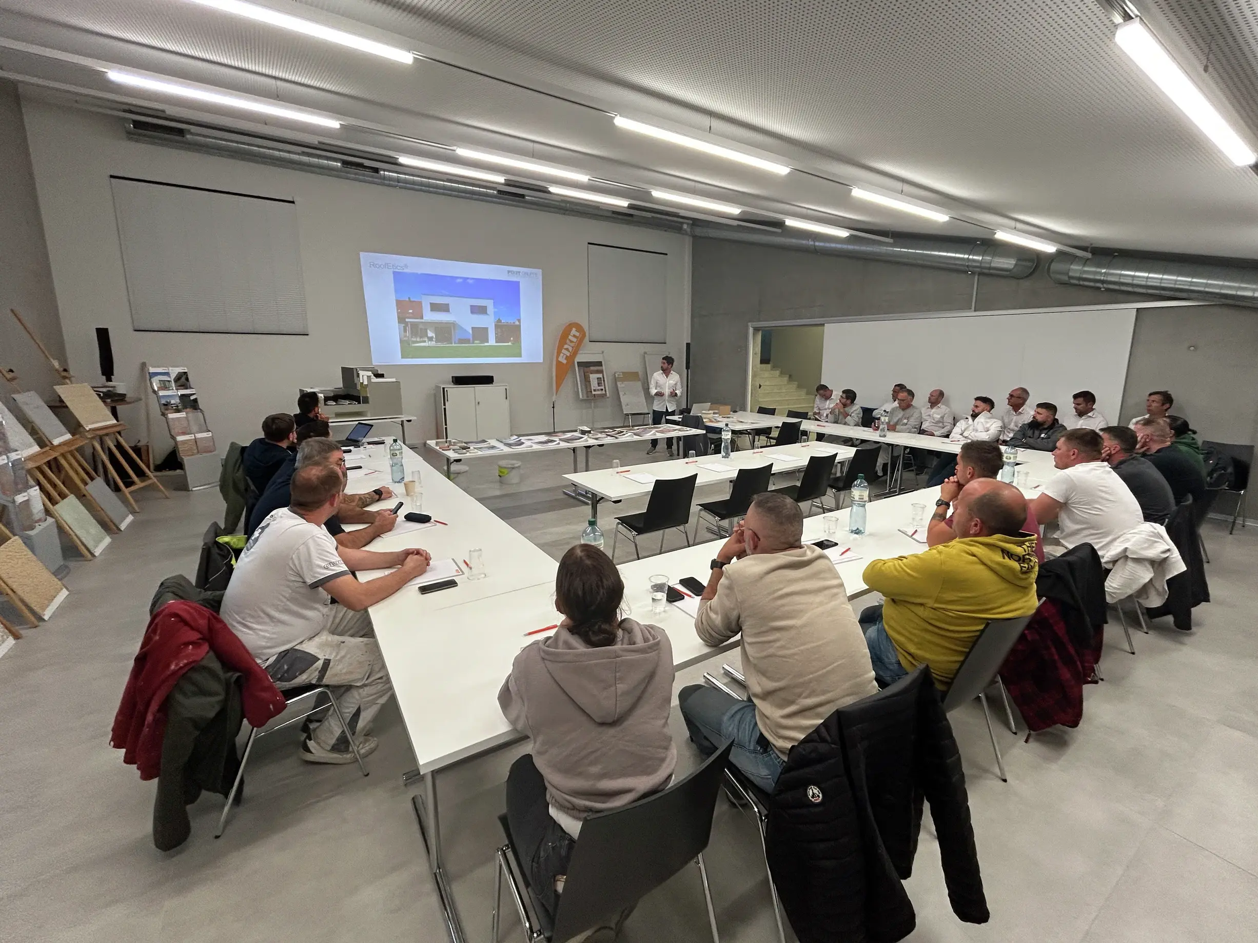 Vue d'ensemble des participants depuis le fond de la salle, avec les diapositives de la présentation en arrière-plan.