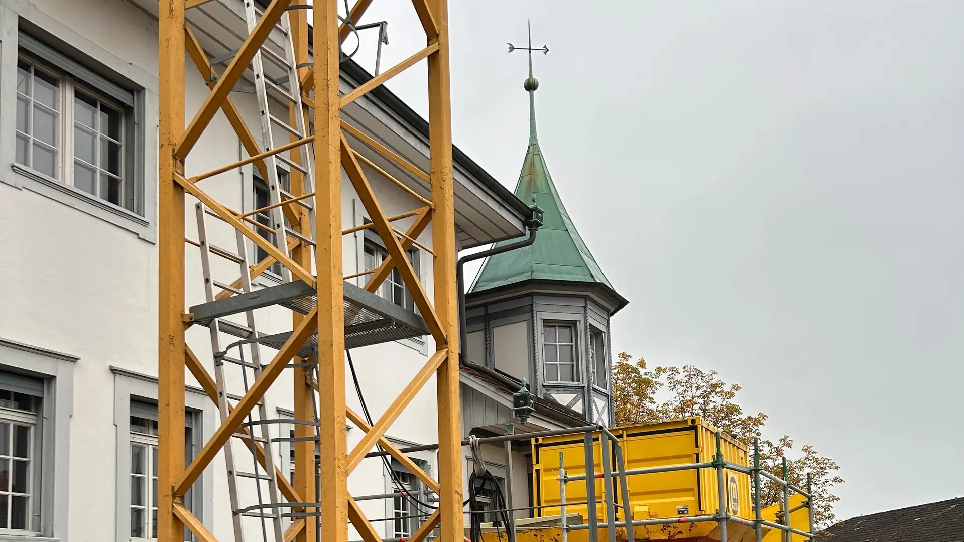 Partie inférieure jaune d'une grue devant un bâtiment historique avec une petite tourelle octogonale au toit de cuivre vert en arrière-plan