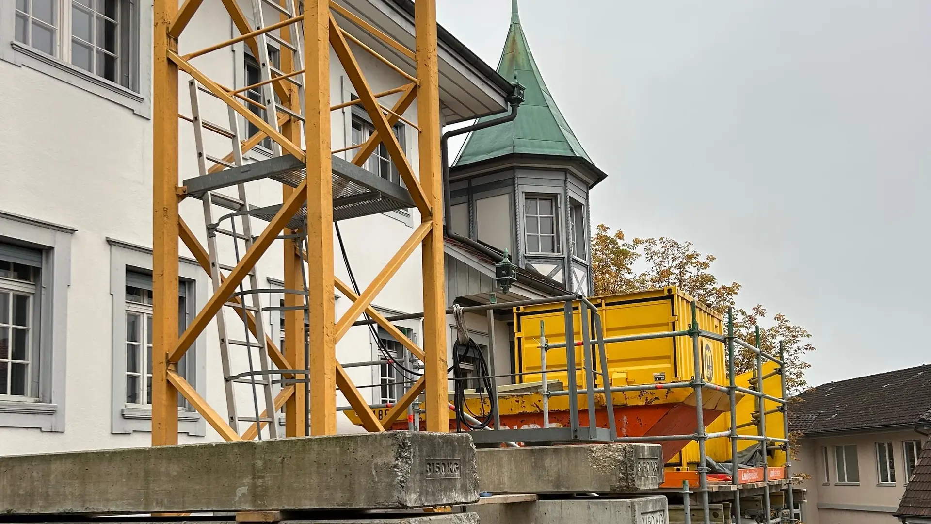 Partie inférieure jaune d'une grue devant un bâtiment historique avec une petite tourelle octogonale au toit de cuivre vert en arrière-plan