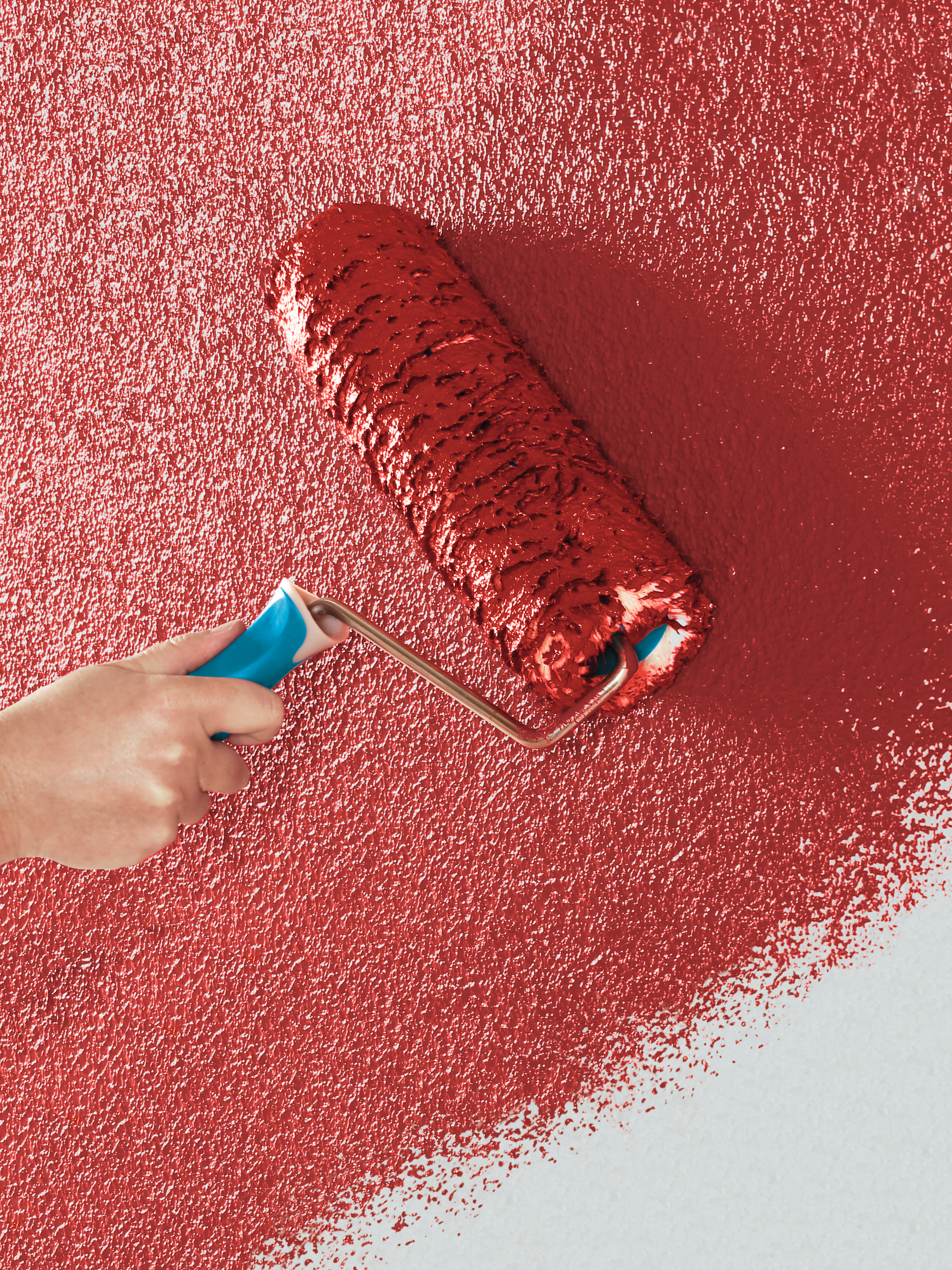 Eine Farbrolle trägt rote Farbe auf eine verputzte Wand auf