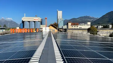 Installation photovoltaïque sur un entrepôt du site de Fixit en Suisse, avec les silos et le bâtiment de production en arrière-plan.