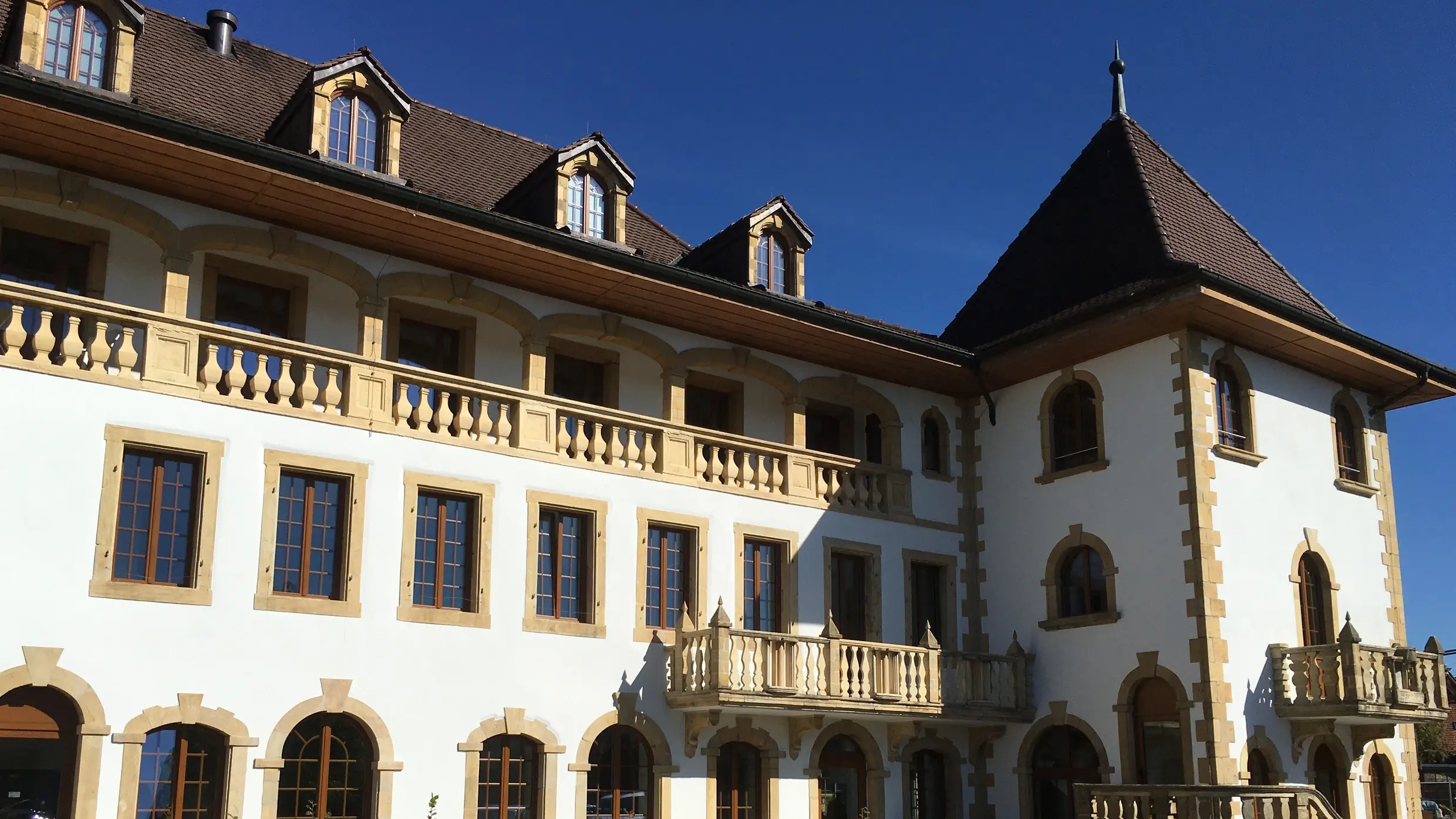 Ein grosses, weiss verputztes und historisches Gebäude mit Sandstein-Rundbögen über den Fenstern und einem Turm