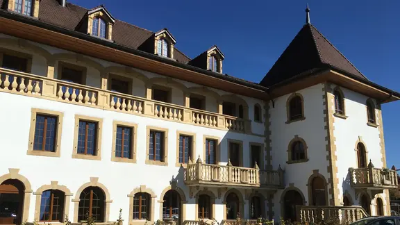Un grand bâtiment historique crépi de blanc avec des arcs en plein cintre en grès au-dessus des fenêtres et une tour