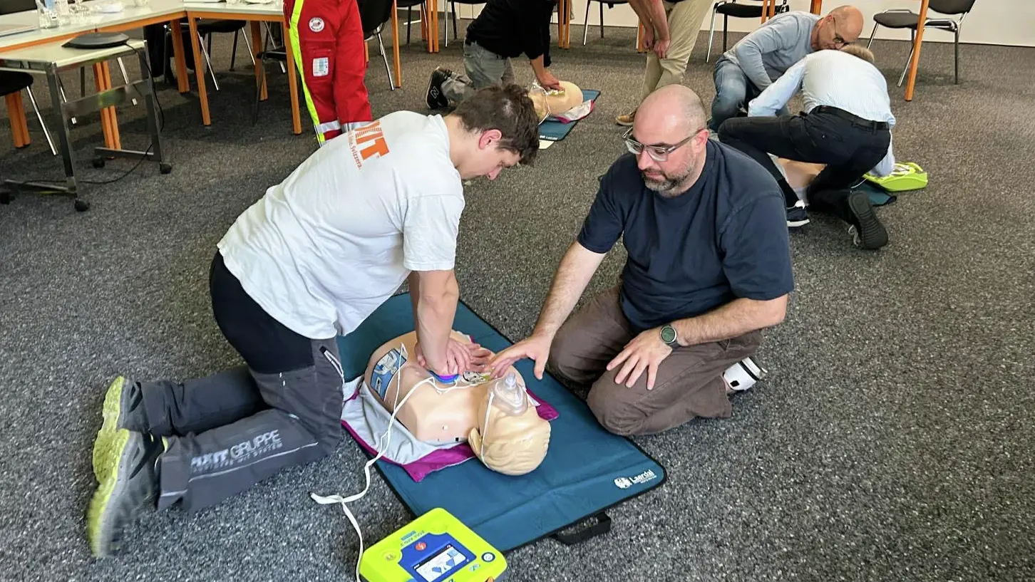Zwei Personen üben die Herzdruckmassage an einer Übungspuppe mit Defibrillator