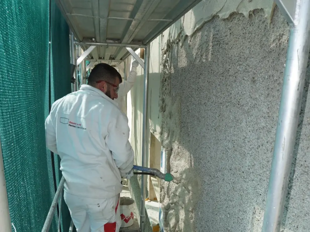 Un artisan applique à la bombe l'enduit isolant Fixit 222 Aerogel sur la façade