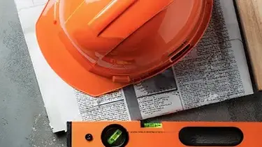 Orangener Bauarbeiterhelm liegt auf einer Zeitung mit einer orangenen Wasserwaage