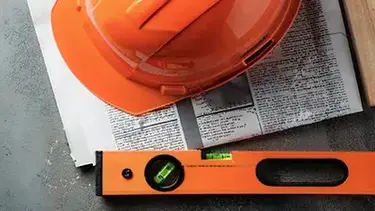 Casque orange d'ouvrier du bâtiment posé sur un journal avec un niveau à bulle orange