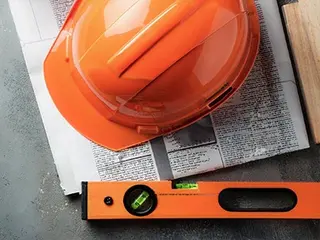 Casque orange d'ouvrier du bâtiment posé sur un journal avec un niveau à bulle orange