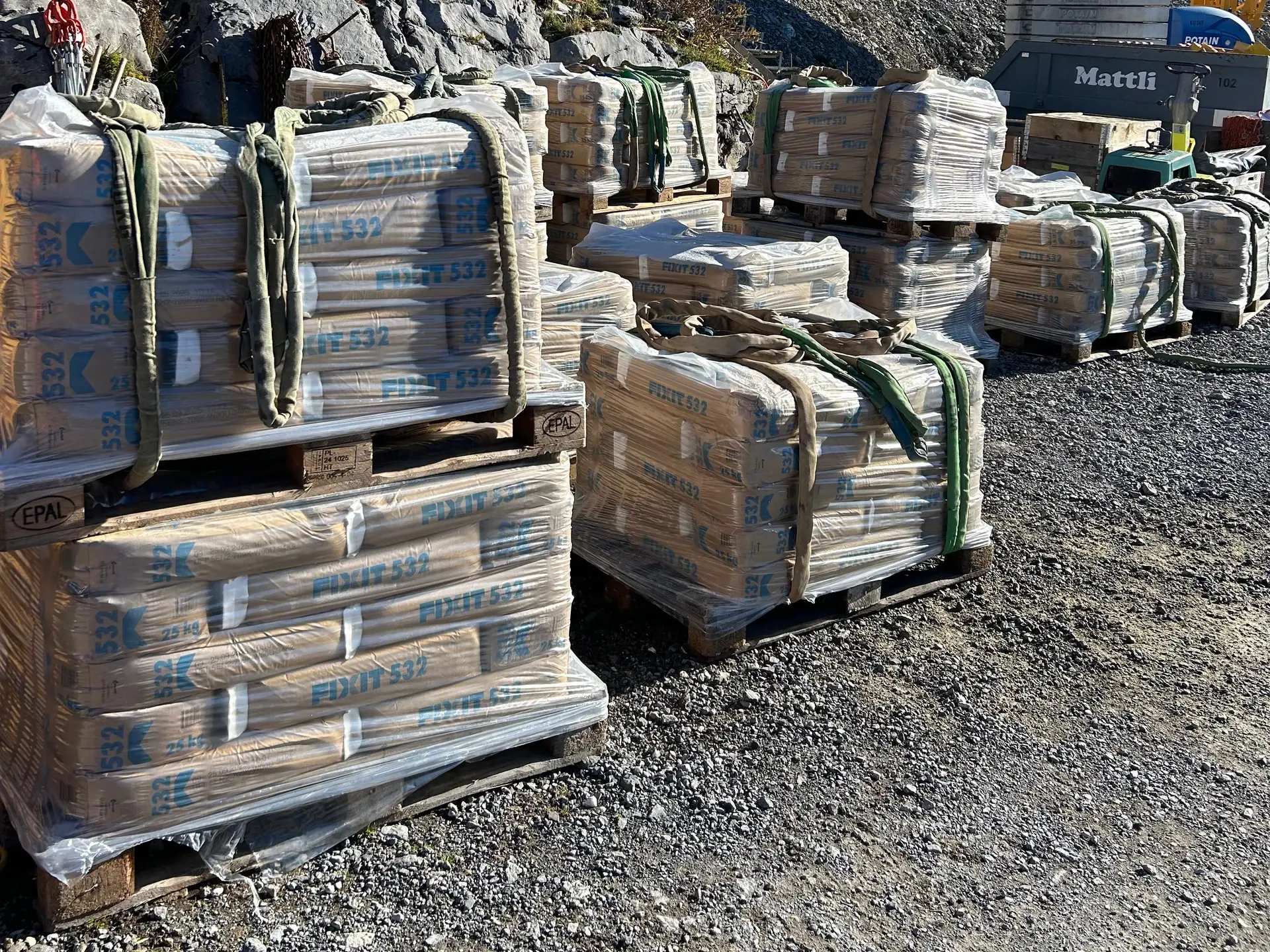 Plusieurs palettes de mortier d'ancrage Fixit 532 sont prêtes à l'emploi sur le chantier, devant une grue jaune