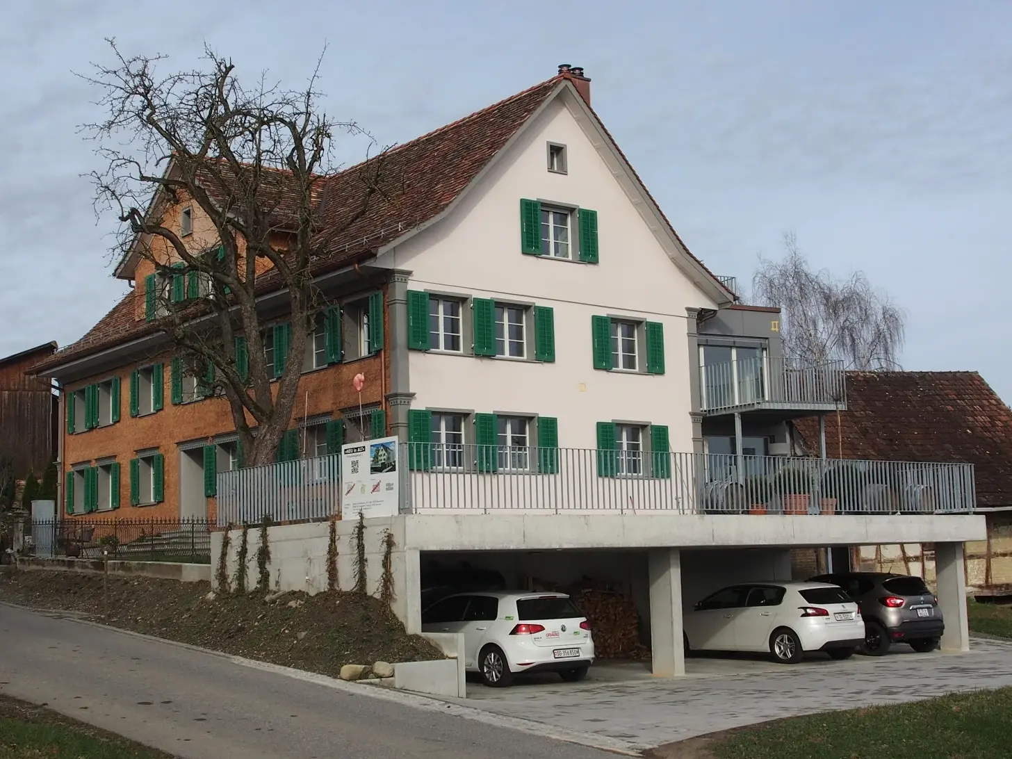 Gesamtansicht des Gebäudes mit dem Carport und der Strasse, sowie der Fassadenseite, die mit Schindeln neu bestückt wurde