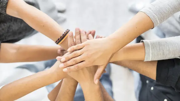 Mehrere Personen legen ihre Hände in der Mitte übereinander, symbolisch für Zusammenhalt