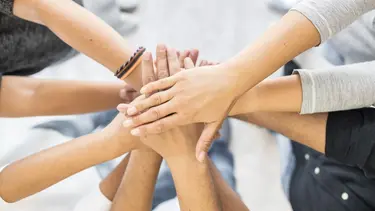 Viele Hände von verschiedenen Personen liegen in der Mitte alle übereinander und symbolisieren Zusammenhalt
