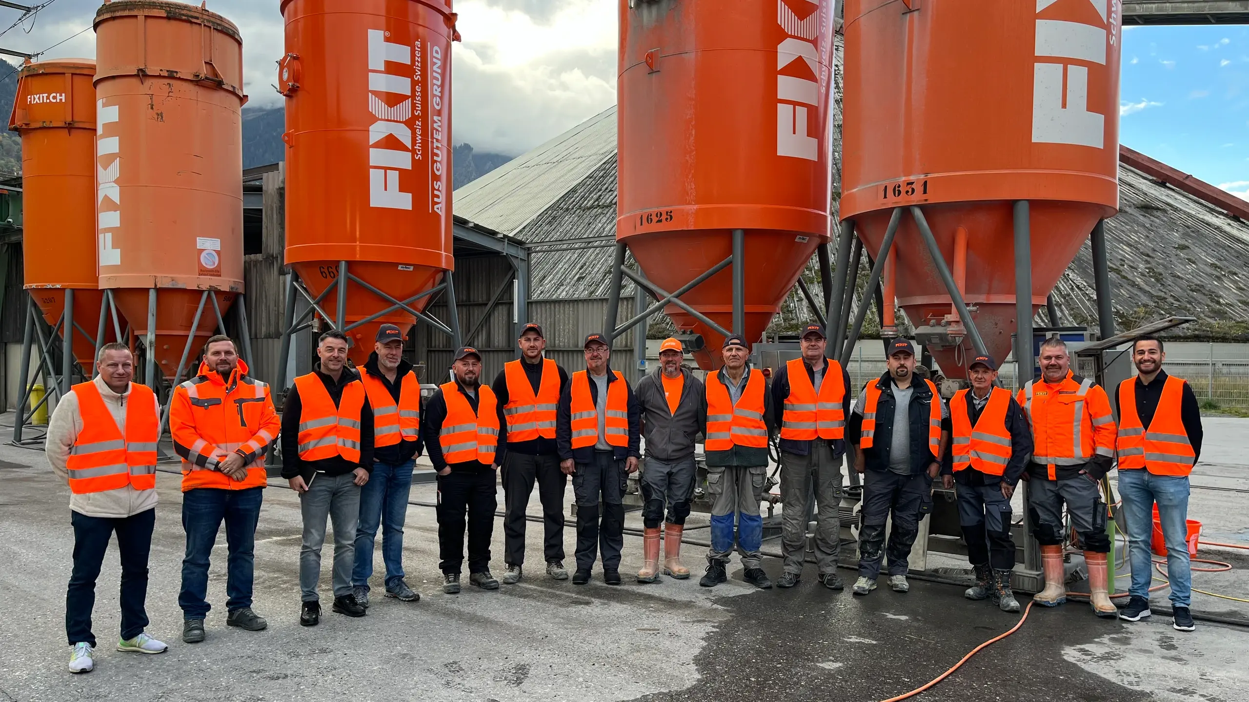 Alle Schulungsteilnehmer und Fixit Mitarbeiter stehen in einem Halbkreis vor diversen, orangenen Fixit Silos
