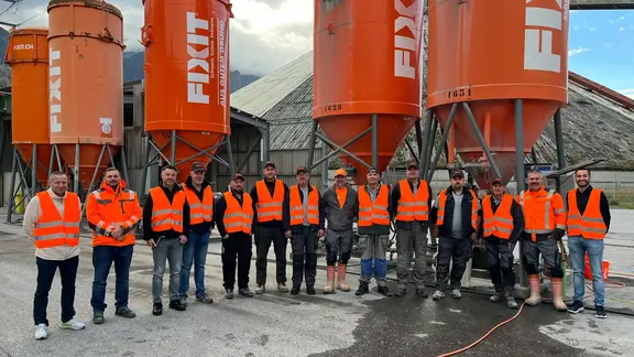 Alle Schulungsteilnehmer und Fixit Mitarbeiter stehen in einem Halbkreis vor diversen, orangenen Fixit Silos
