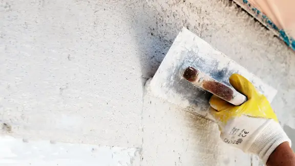 Hand mit Kelle verspachtelt die Wand