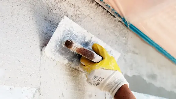 [Translate to Deutsch:] Hand mit Kelle verspachtelt die Wand